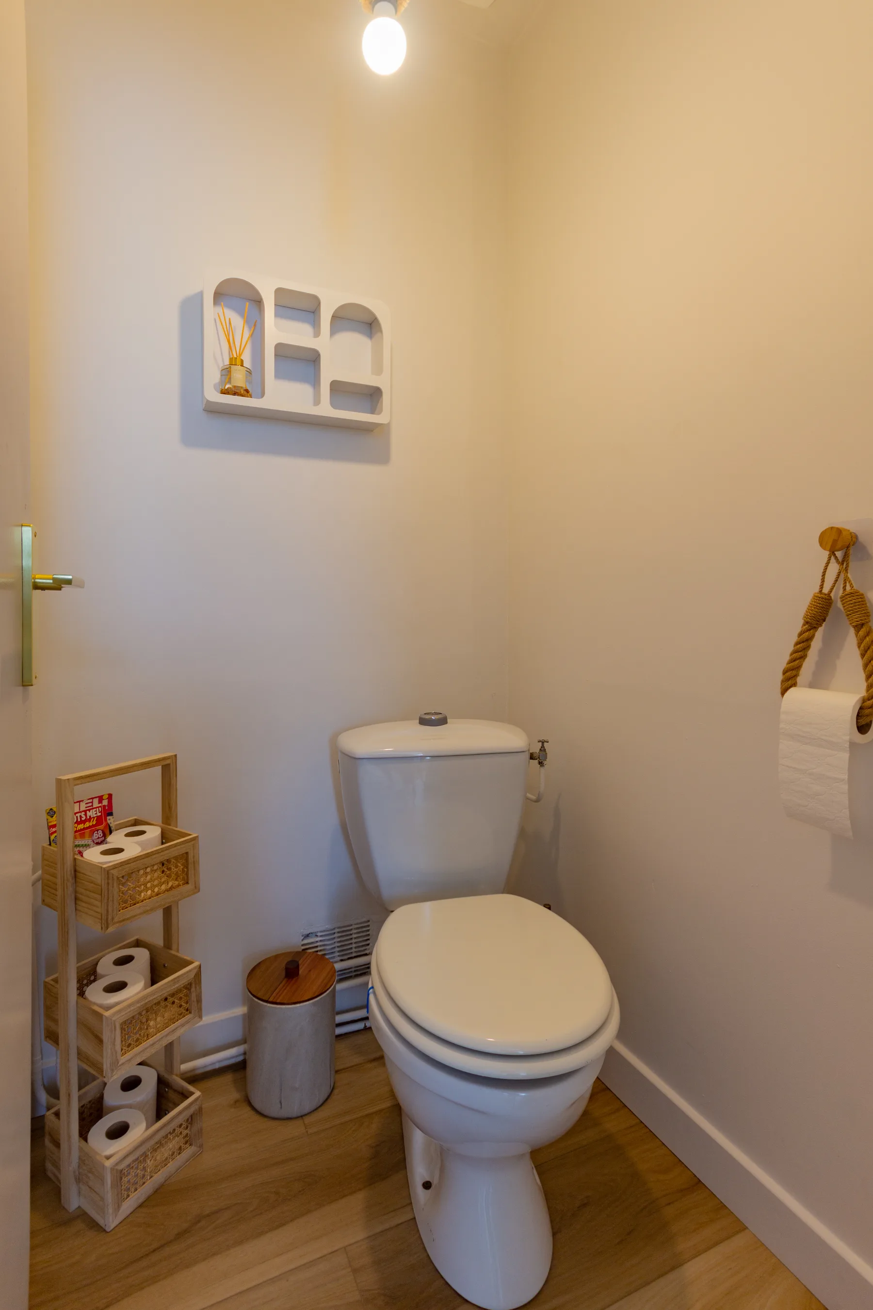 WC après rénovation avec murs clairs, sol bois et accessoires de rangement
